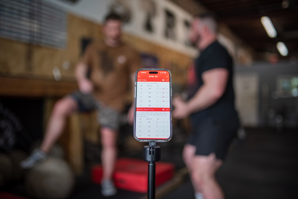 Trainer App on a phone in the gym displaying workout tracking for upper day lifts